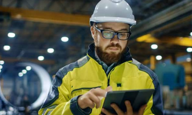 Worker wearing white hard hat looking at tablet.