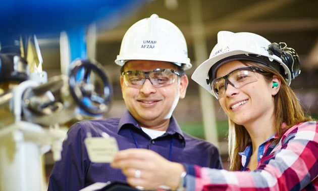 Two workers wearing hard hats looking at a report.