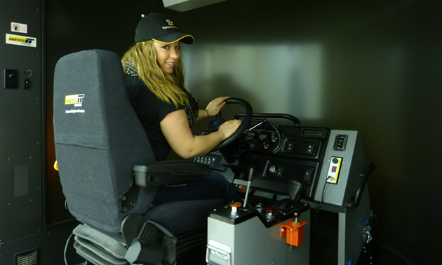 A blonde-haired women sitting in the haul truck simulator.